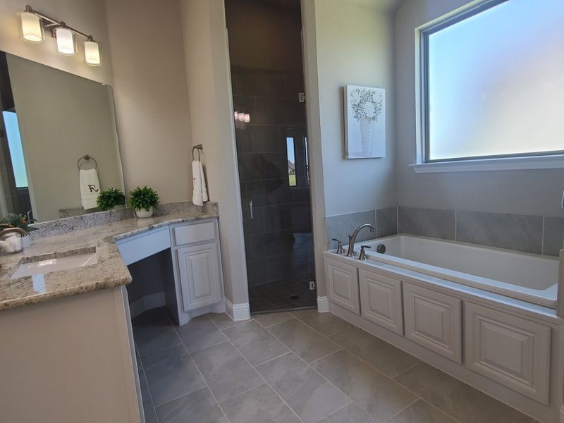 A modern bathroom featuring a granite-topped vanity, spacious tub, and stylish lighting.