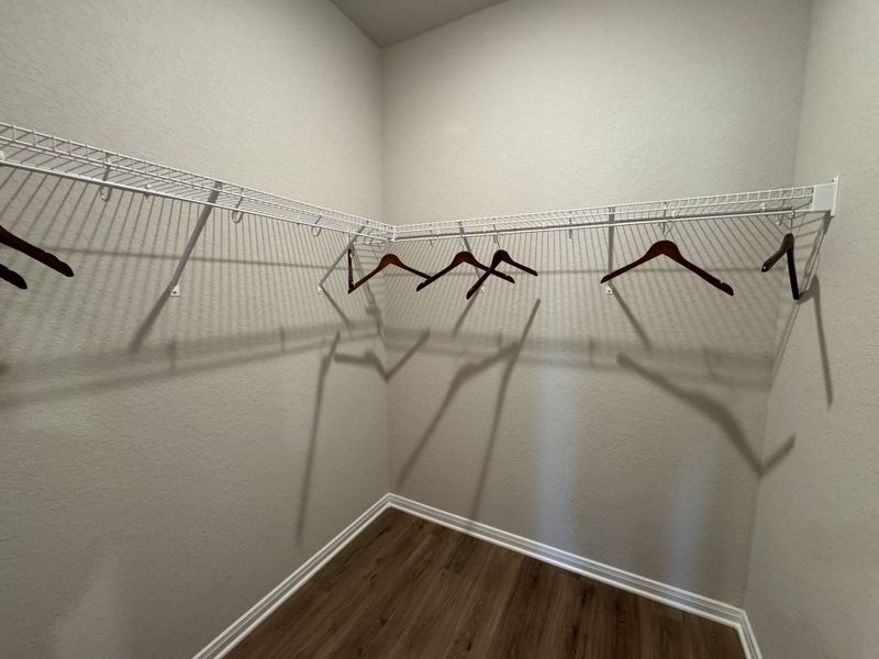 A spacious walk-in closet with wooden hangers and sleek wire shelving, accented by warm-toned flooring.