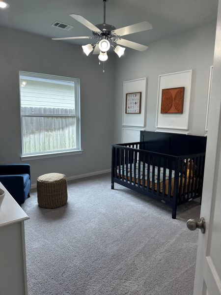 A cozy nursery with soft carpet, a navy crib, and modern ceiling fan, accented by framed wall art and natural light. A cozy nursery with soft carpet, a navy crib, and modern ceiling fan, accented by framed wall art and natural light.