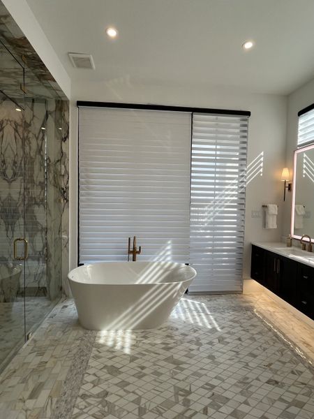 A luxurious bathroom features a freestanding tub, marble floors, and a glass shower with elegant tile work.