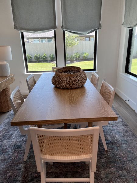 A cozy dining area with a wooden table, woven chairs, and large windows providing natural light and garden views.