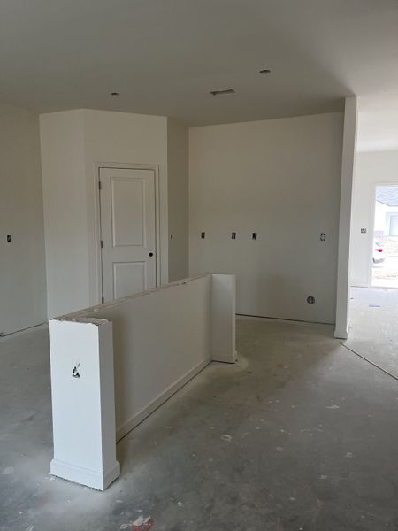 A spacious room under construction with simple white walls, a low dividing wall, and a closed door in the background.
