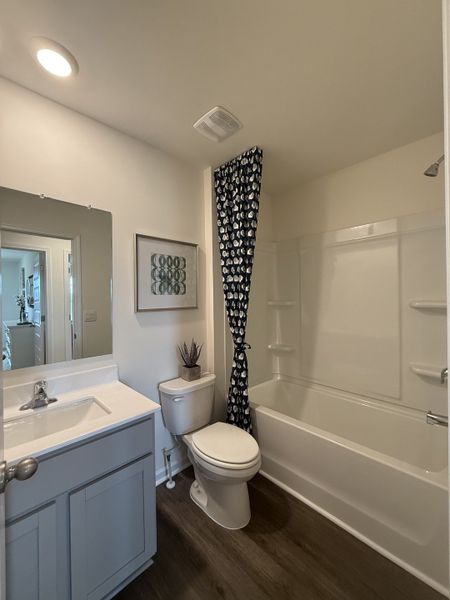 A cozy bathroom featuring a shower-tub combo, sleek vanity, and patterned curtain.