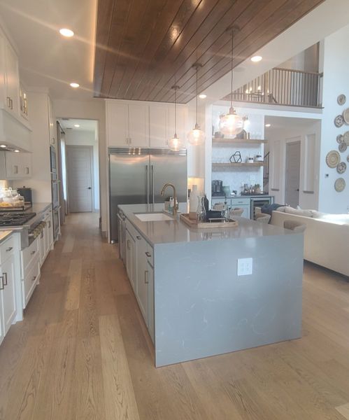 A spacious kitchen with sleek gray island, wood ceiling accents, pendant lighting, and modern appliances.