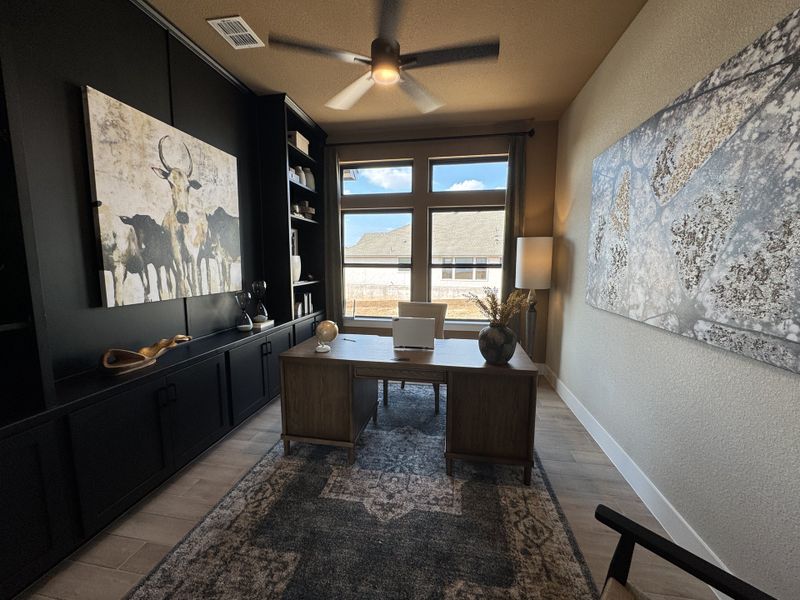A sophisticated home office with sleek black cabinetry, large art pieces, and a windowed wall for natural light.