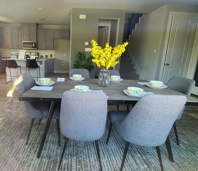 A modern dining area with gray chairs, a rustic table, and vibrant floral centerpiece, connected to a sleek kitchen. A modern dining area with gray chairs, a rustic table, and vibrant floral centerpiece, connected to a sleek kitchen.