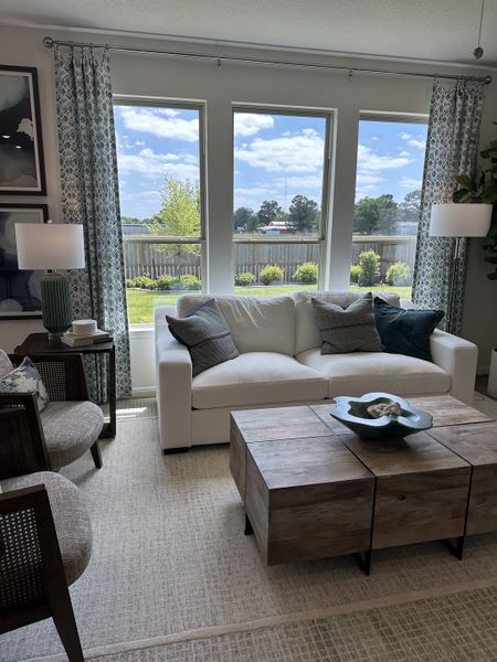 A cozy living room with a white sofa, rustic wooden table, and large windows offering a serene view.