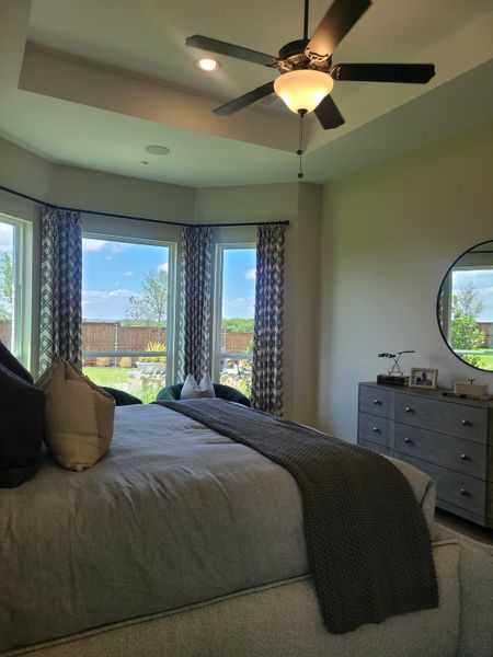 A cozy bedroom featuring large bay windows, elegant drapery, a ceiling fan, and a stylish dresser. A cozy bedroom featuring large bay windows, elegant drapery, a ceiling fan, and a stylish dresser.