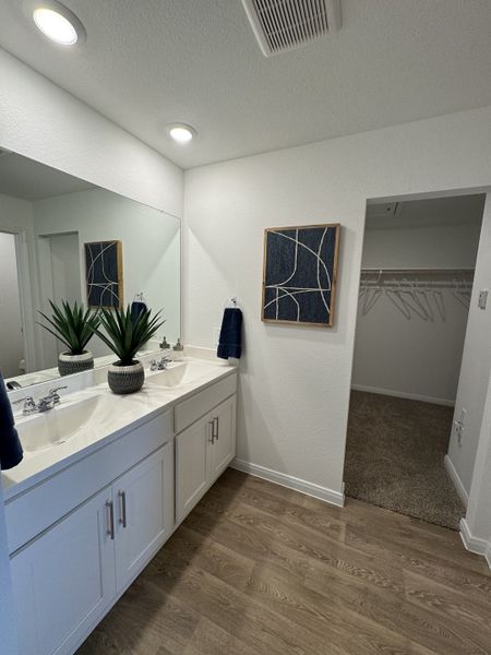A modern bathroom with dual sinks, sleek white cabinets, stylish wall art, and warm wood flooring. A modern bathroom with dual sinks, sleek white cabinets, stylish wall art, and warm wood flooring.