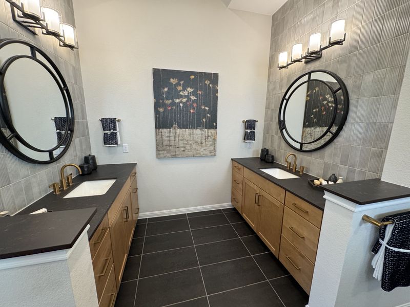 A contemporary bathroom featuring dual wooden vanities, round mirrors, and elegant lighting fixtures.