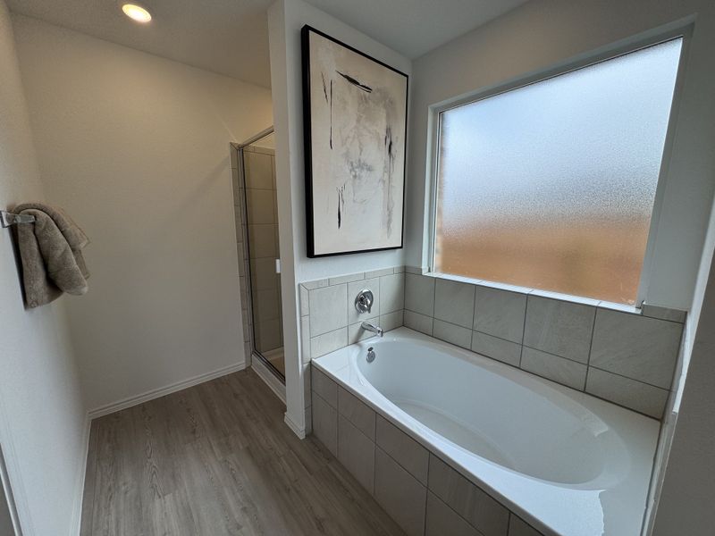 A modern bathroom with a tiled bathtub, frosted window, sleek shower, and elegant artwork for a serene escape.