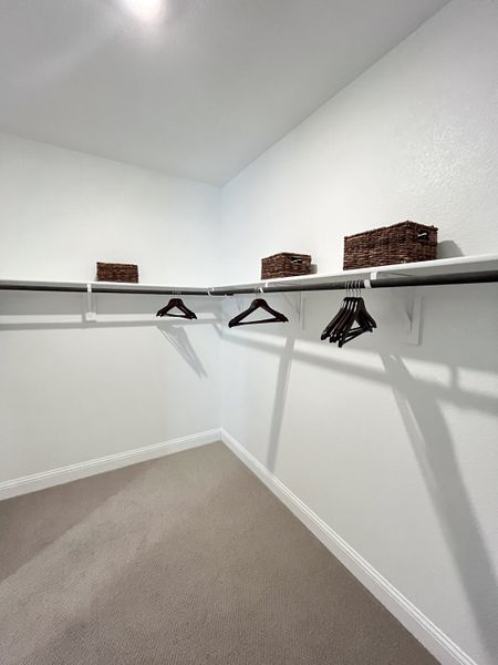 A spacious walk-in closet with white walls, carpeted flooring, and organized shelving.