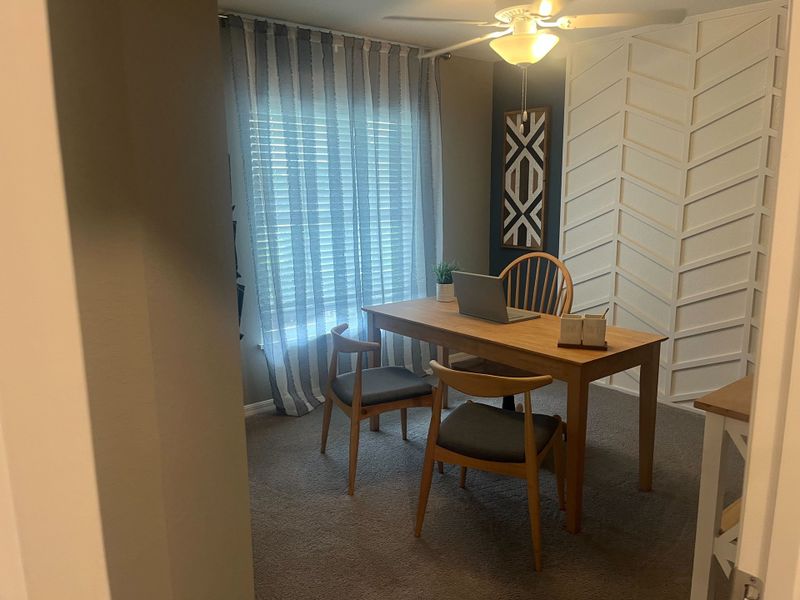A cozy office with a wooden desk, modern chairs, striped curtains, and stylish wall decor.