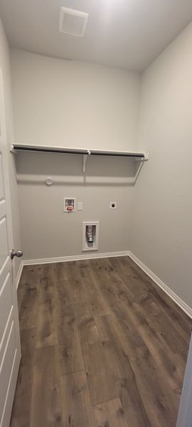 A bright laundry room with sleek wooden flooring, a built-in shelf, and washer-dryer connections.