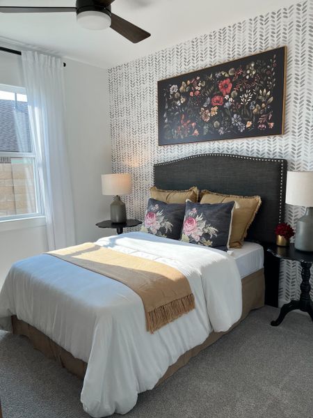 A cozy bedroom with floral accents, patterned wallpaper, and elegant bedding, showcasing modern and chic decor.