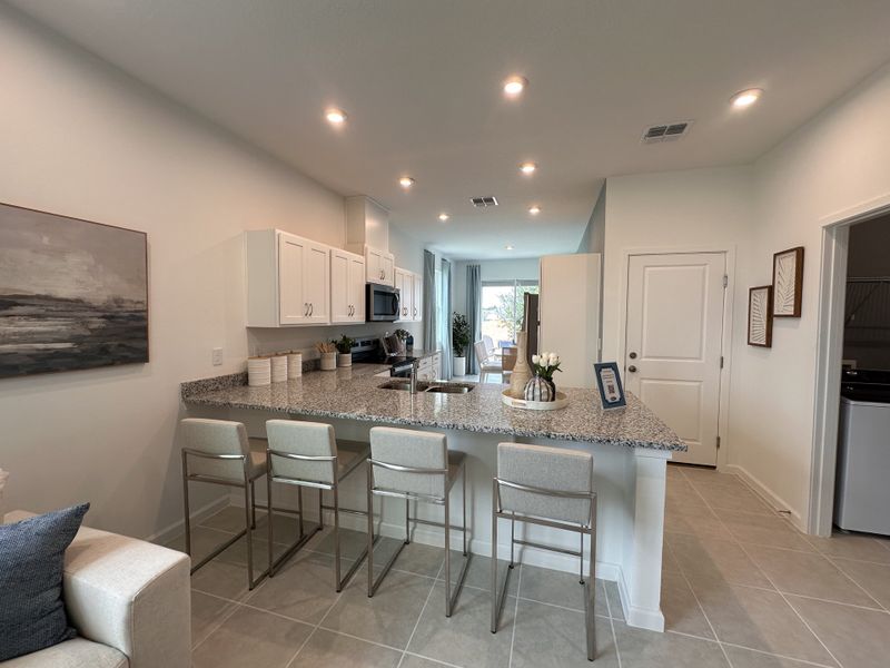 A modern kitchen with granite countertops, sleek white cabinets, and bar seating, complemented by recessed lighting.