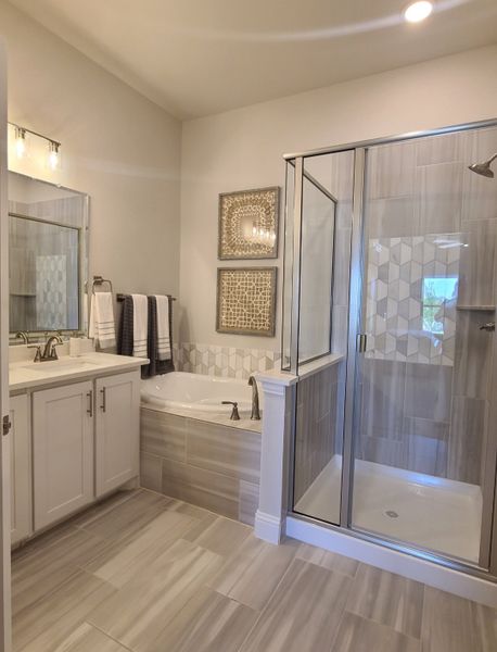A modern bathroom with sleek tile flooring, a glass shower, tub, and elegant lighting.