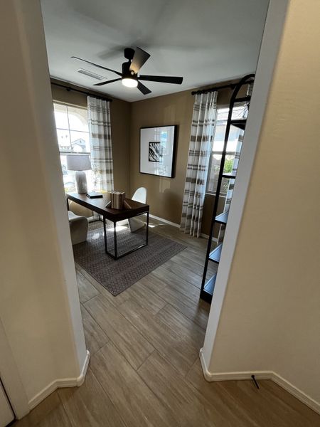 A modern office space with wood flooring, large windows, and a sleek black fan, creating a warm and inviting workspace.