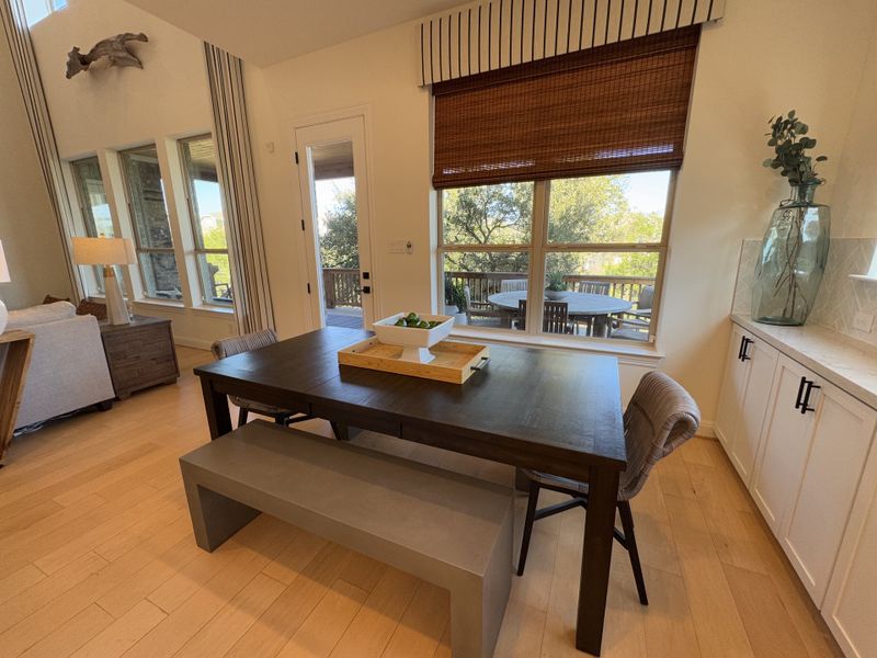 A cozy dining area with a dark wood table, stylish bench, and view of a lush backyard through large windows. A cozy dining area with a dark wood table, stylish bench, and view of a lush backyard through large windows.