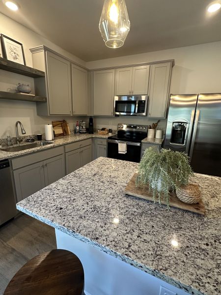 A modern kitchen featuring granite countertops, gray cabinets, and stainless steel appliances with stylish lighting.