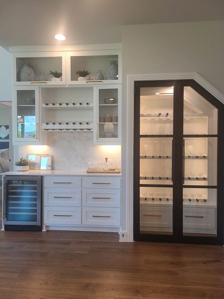 A chic home bar with elegant glass cabinets, a wine cooler, and warm wood flooring.