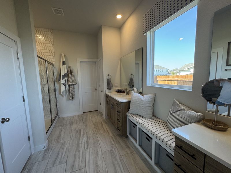 A spacious bathroom with dual vanities, a tiled shower, and cozy seating under a large window, featuring modern decor. A spacious bathroom with dual vanities, a tiled shower, and cozy seating under a large window, featuring modern decor.