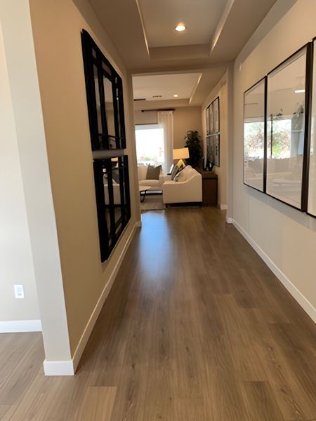 A modern hallway with sleek wood flooring, recessed lighting, and wall art leading to a cozy living space.