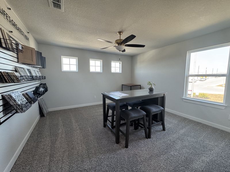 A bright design room with carpeted flooring, a high table with stools, and a display of sample materials on the wall. A bright design room with carpeted flooring, a high table with stools, and a display of sample materials on the wall.