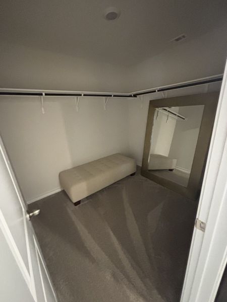 A spacious walk-in closet with plush carpet, a large mirror, and a cushioned bench for added luxury and convenience.