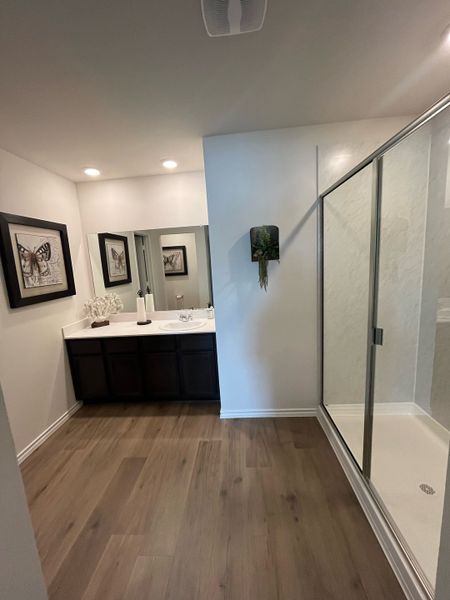 A sleek bathroom featuring a spacious glass shower, wooden flooring, and elegant dark cabinetry.