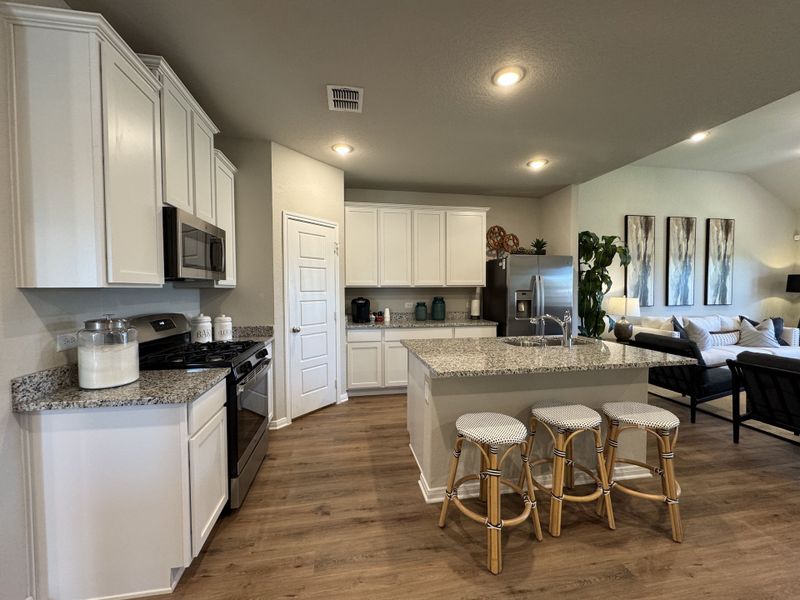 A modern kitchen with white cabinets, granite countertops, and a spacious island leading into a cozy living area.