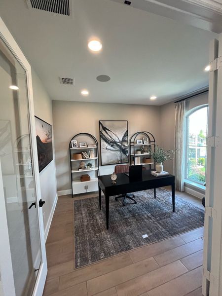 A modern home office with sleek black desk, stylish bookshelves, and large window offering natural light.