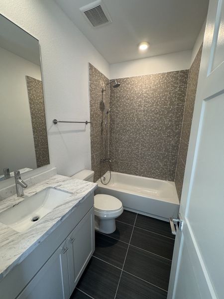 A modern bathroom featuring a marble-topped vanity, patterned tile shower, and sleek dark floor tiles. A modern bathroom featuring a marble-topped vanity, patterned tile shower, and sleek dark floor tiles.