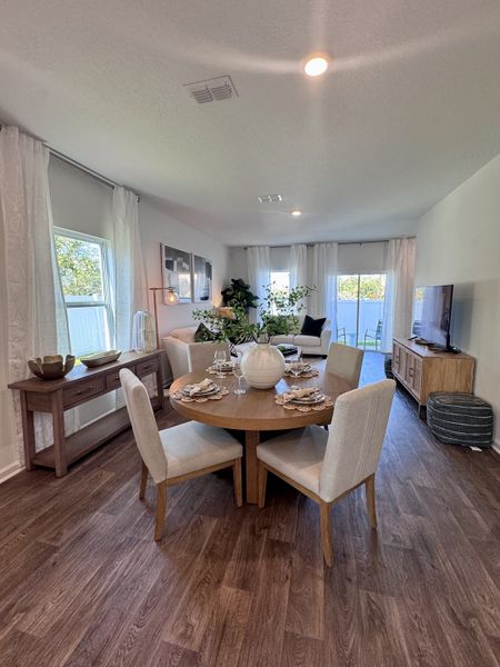An elegant dining area with a round wooden table, chic decor, and warm wood flooring, creating a cozy, inviting atmosphere.
