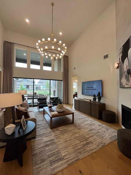 A spacious living room featuring a stylish chandelier, cozy seating, and expansive windows overlooking a lush backyard. A spacious living room featuring a stylish chandelier, cozy seating, and expansive windows overlooking a lush backyard.