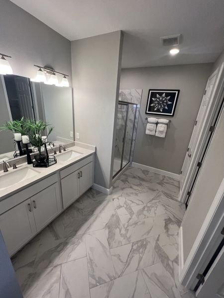 A chic bathroom showcasing marble-patterned tiles, dual sinks, a glass shower, and modern decor.