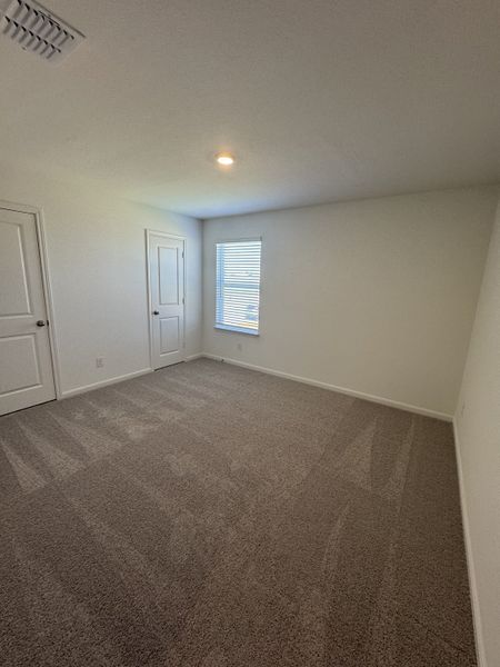 A spacious bedroom with soft carpeting, neutral walls, a window, and a double-door closet for ample storage.