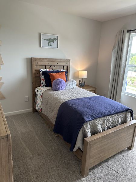A cozy bedroom with dinosaur-themed decor, natural wood bedframe, plush bedding, and soft lighting.