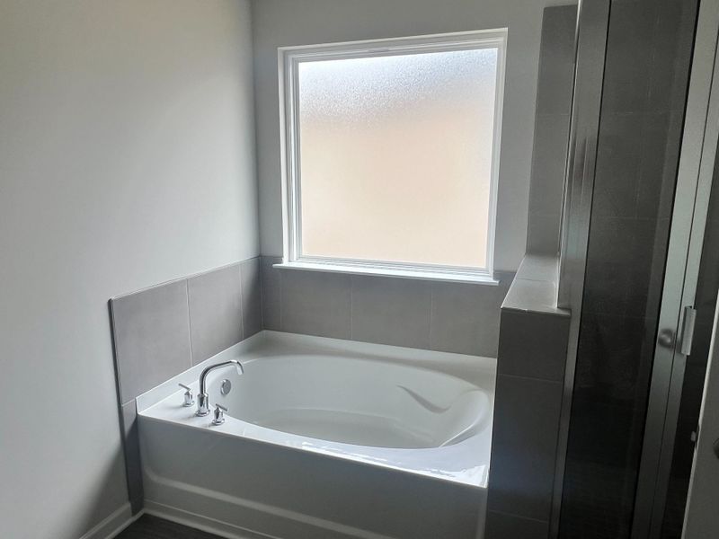 A sleek bathroom featuring a modern bathtub with gray tiles and a frosted window, creating a serene retreat. A sleek bathroom featuring a modern bathtub with gray tiles and a frosted window, creating a serene retreat.
