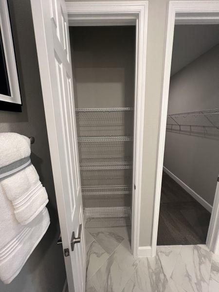 A sleek storage area with white shelving, adjacent to elegant marble-tiled flooring and modern towel display.