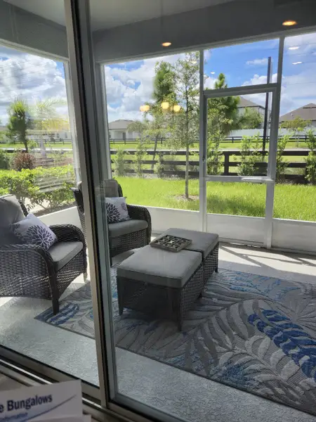 A cozy sunroom with wicker seating, a patterned rug, and lush greenery views through large windows.
