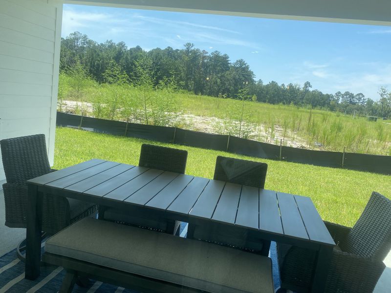 A cozy patio area with a sleek dark table and woven chairs, overlooking a lush green lawn and scenic natural views.