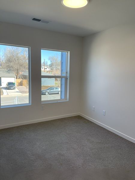 A bright upstairs bedroom with large windows, plush carpeting, and a neutral palette for a fresh and airy feel.