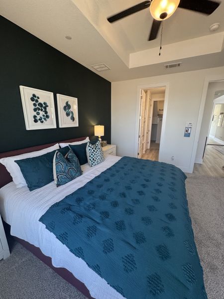 A cozy bedroom with dark accent wall, elegant bedding, and modern ceiling fan.