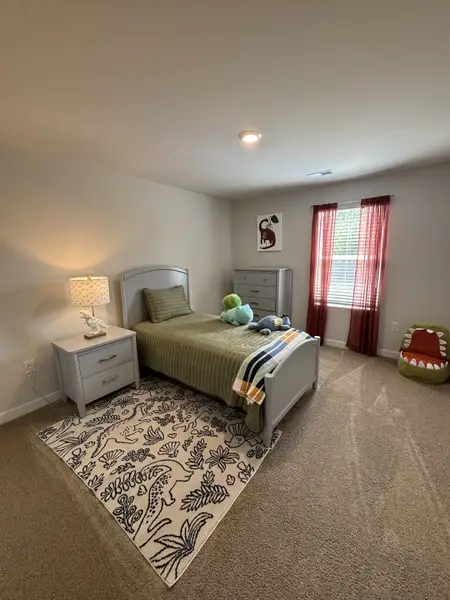 A cozy child's bedroom with an olive bedspread, dinosaur-themed rug, and bright decor accents. A cozy child's bedroom with an olive bedspread, dinosaur-themed rug, and bright decor accents.