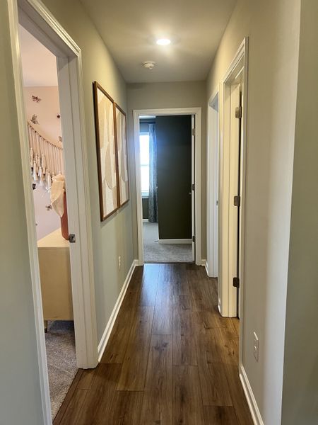 A cozy hallway with wooden flooring, soft lighting, and tasteful wall art leading to inviting rooms.
