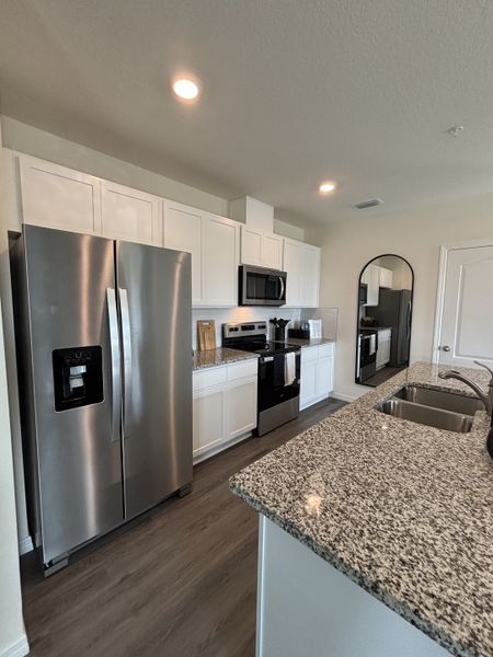 A modern kitchen with sleek granite countertops, stainless steel appliances, and white cabinetry in Avian Pointe Townhomes by D.R. Horton (Apopka, FL).