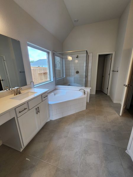 A bright bathroom featuring a spacious corner bathtub, sleek white cabinetry, and modern tile flooring.