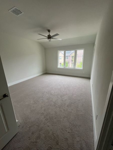 A bright, spacious bedroom with plush carpet, ceiling fan, and large window for natural light.