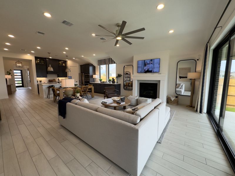 An open-concept living room with sleek flooring, modern kitchen, and cozy seating area, enhanced by large windows and elegant lighting.